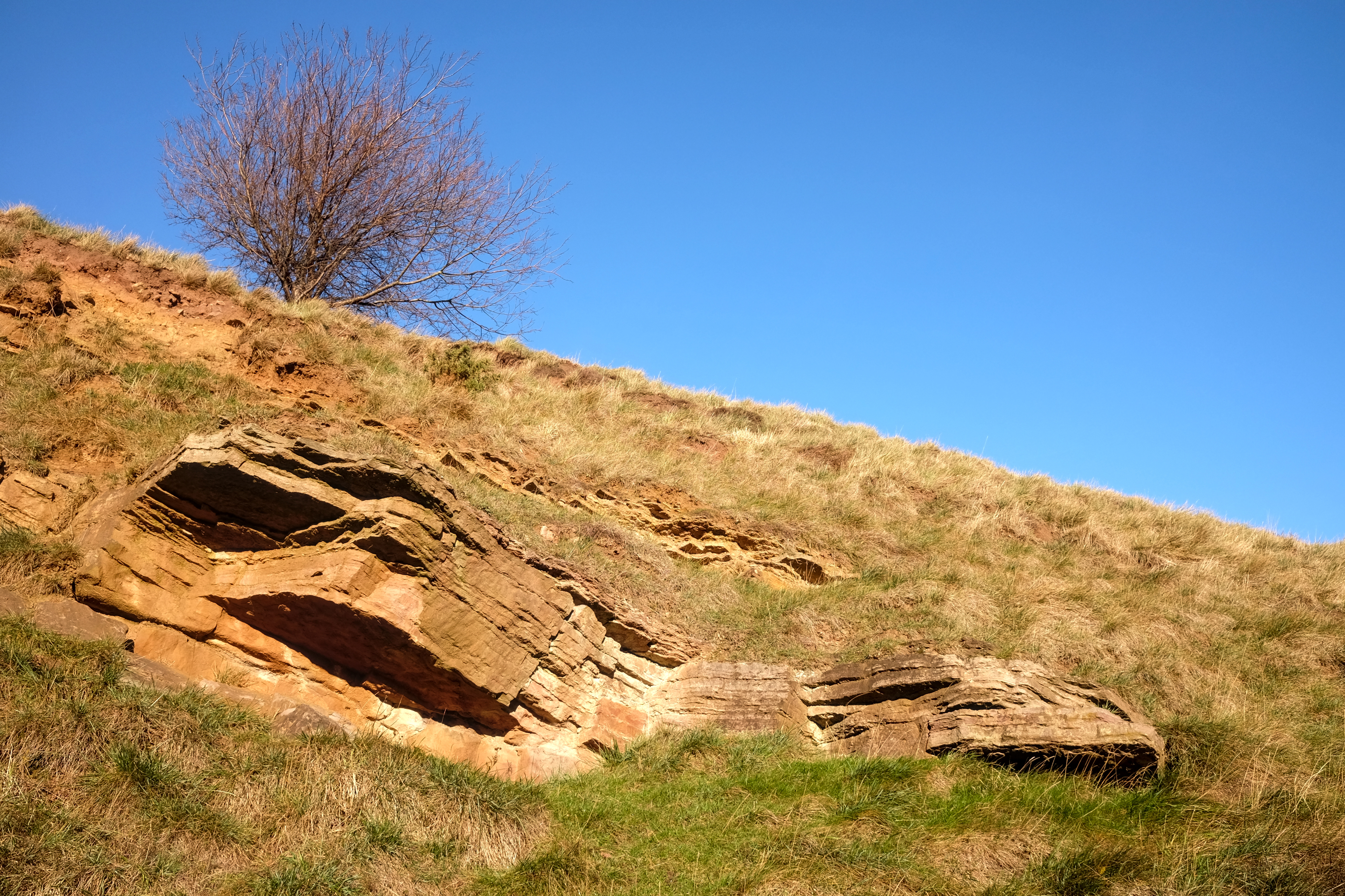 A photo of a layered rock formation against a blue sky.